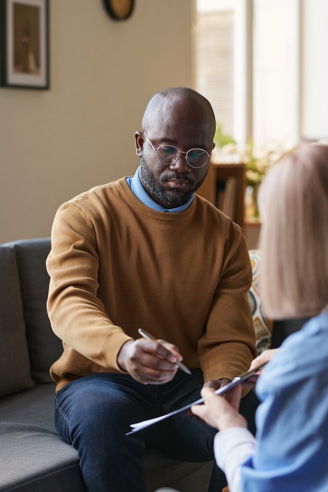 Vertical portrait of adult man signing psychotherapy assessment on clipboard for psychiatric care
